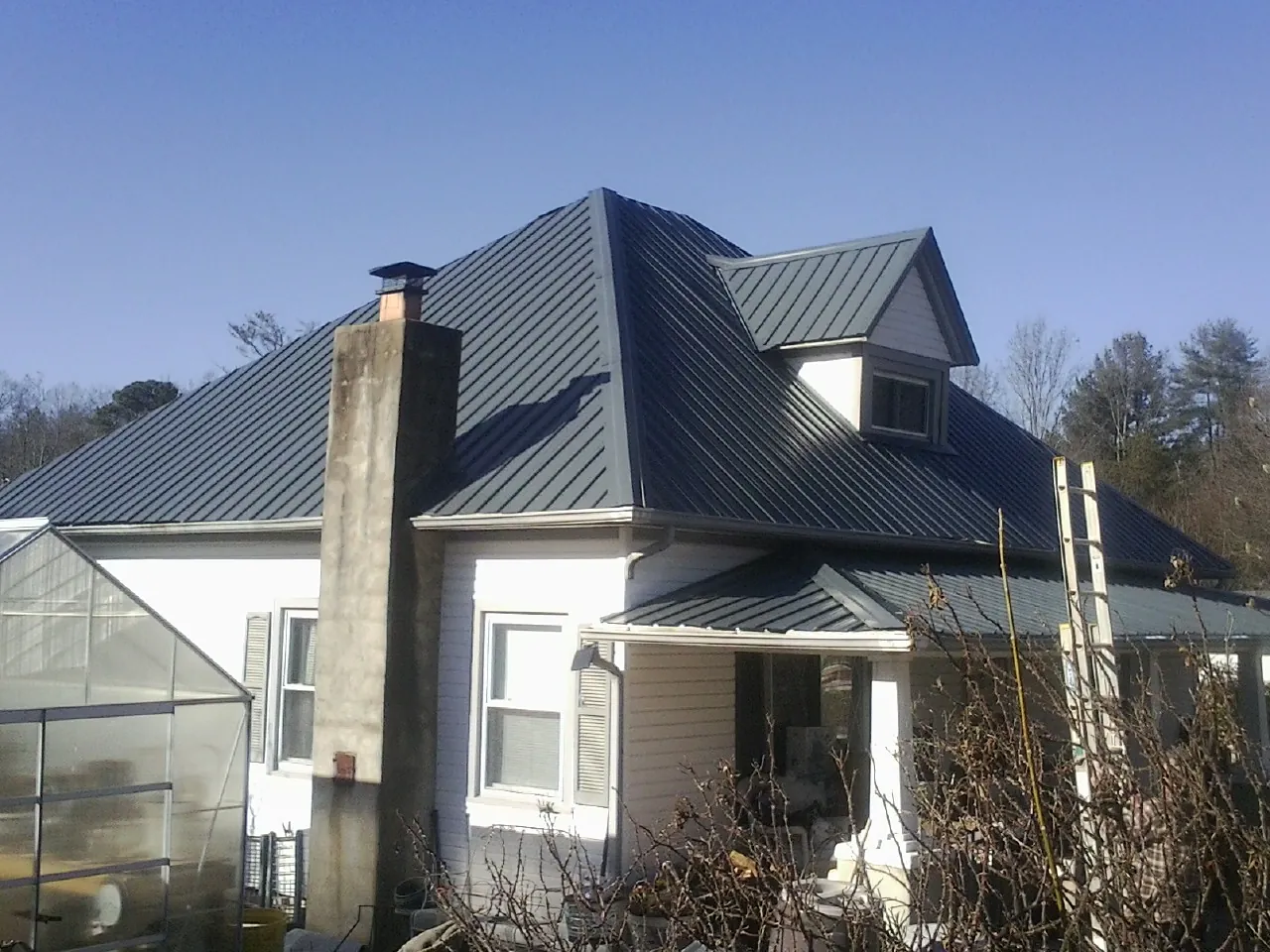 Dark blue standing seam metal roof on a white farmhouse with dormer — Slate & Tile Roof Repair by Roofing Brothers in Lockport