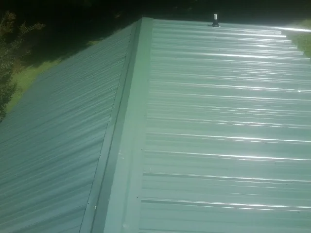 New green metal panels meeting at the ridge of a roof — Flat Roof Repair work by our crew in Lockport