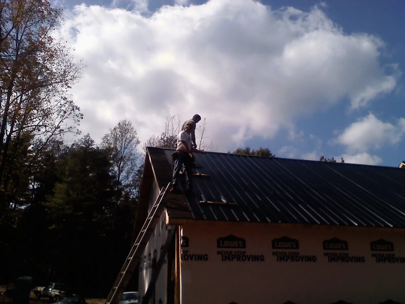 Roofer fastening dark metal panels high against a cloudy sky in Lockport